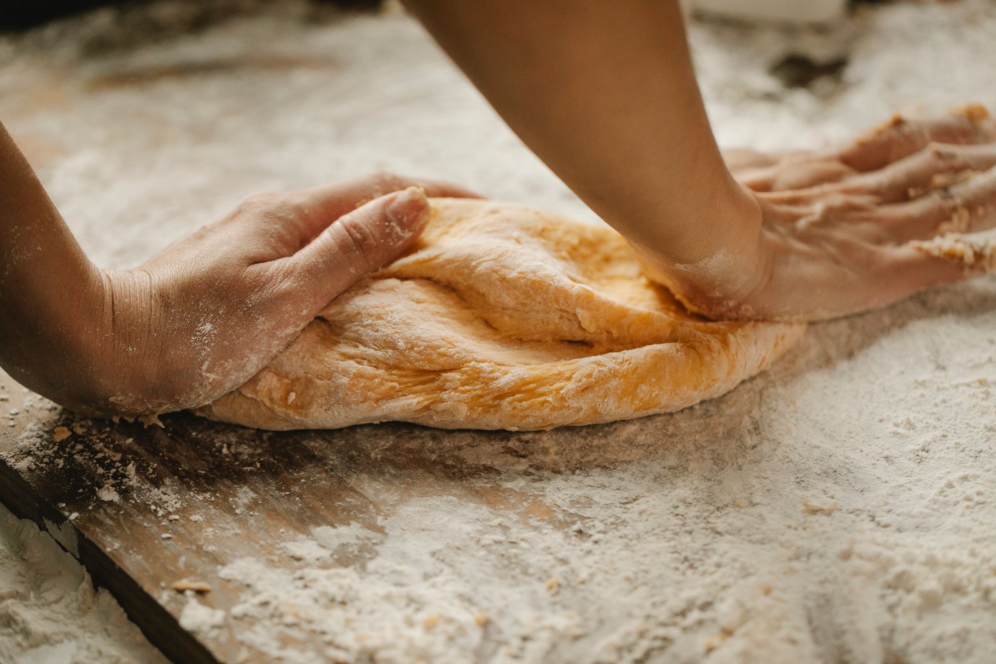 Mains qui travaillent la pâte sur une table en bois couverte de farine